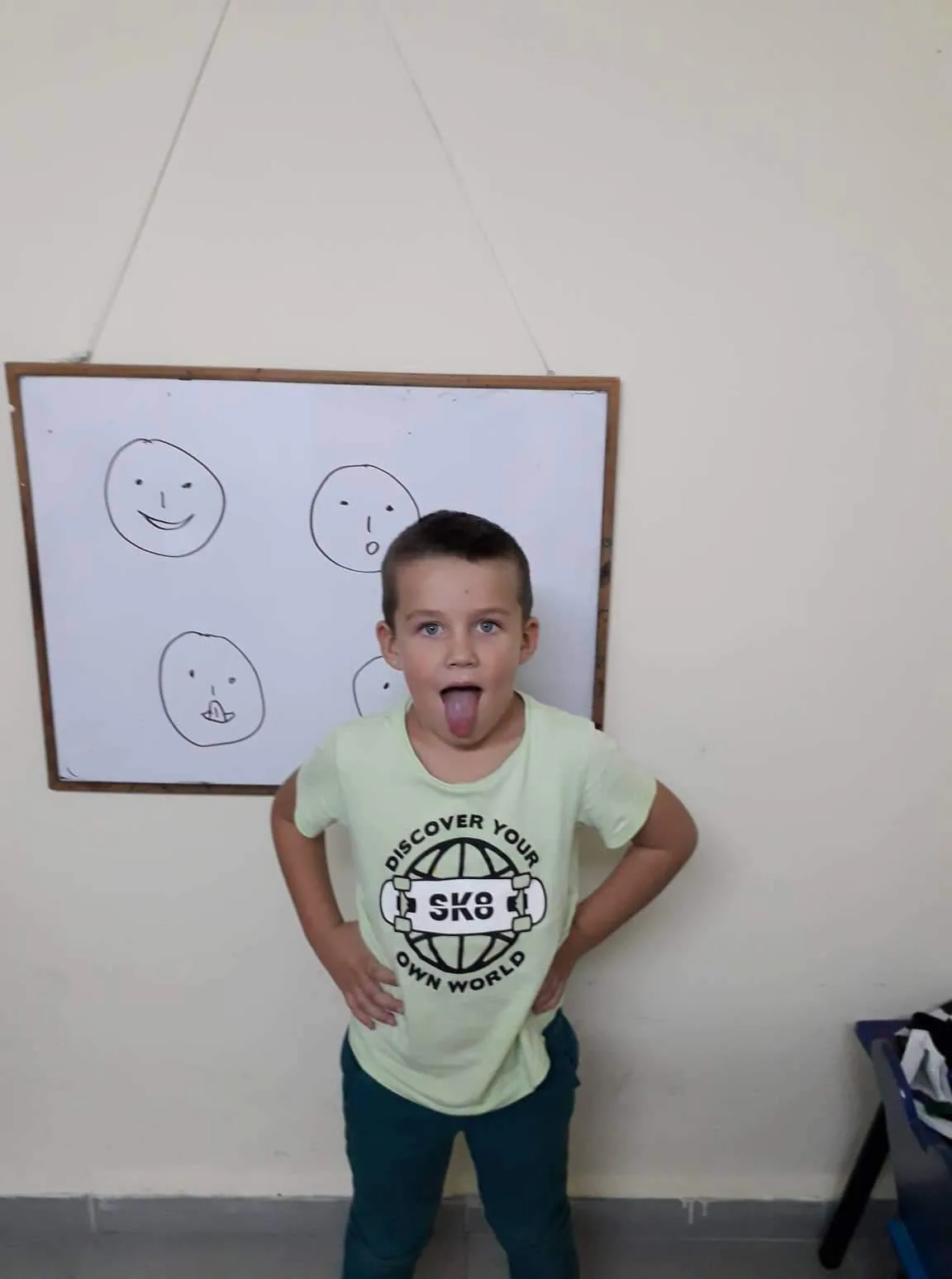 ילד מתרגל תרגיל לשון ליד לוח עם פרצופים