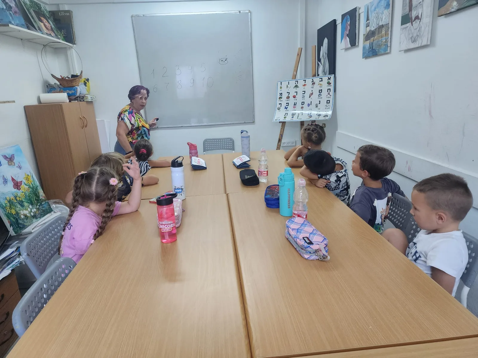 שיעור הכנה לכיתה א׳: הילדים סביב השולחן והמורה ליד הלוח